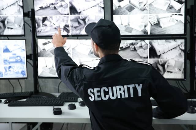 security guard looking at multiple computer screens pointing at image on screen