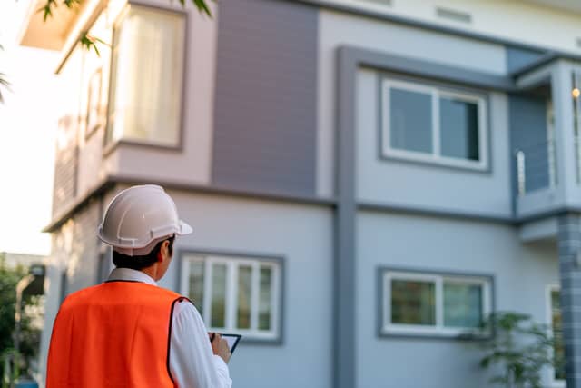 man with orange vest and white hard hat looking up at residential building